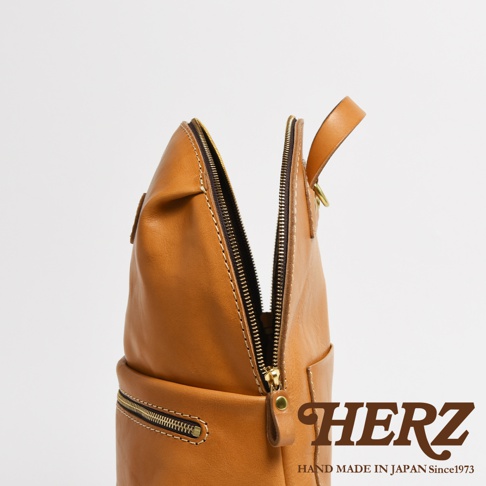 職人手作皮革大開口圓角後背包，採用光滑棕色皮革，設有金色拉鍊和圓形提把，展現簡約設計。