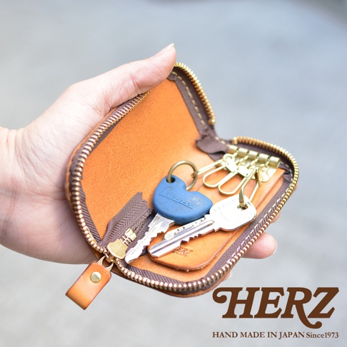 手持一個棕色皮革鑰匙包，裡面裝有四把鑰匙，其中一把藍色鑰匙的形狀獨特。