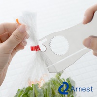 銀色金屬材質的萬用開罐器，一端有兩個小叉子，另一端有一個鋸齒狀的圓形開口，正被用來開啟塑膠袋。