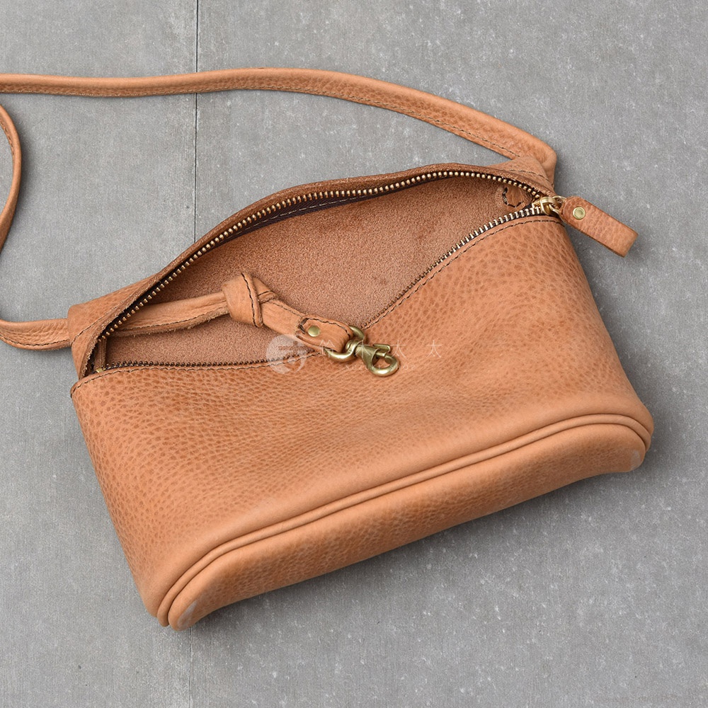 淺棕色皮革製成的斜背包，帶有拉鍊開口和金屬掛鉤。