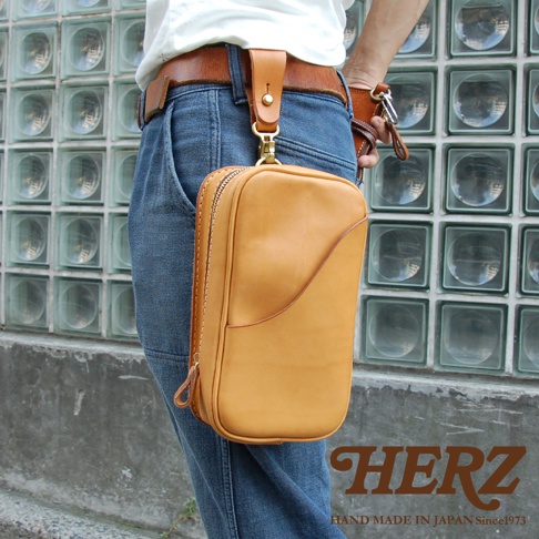 日本HERZ職人手作皮革兩用直立型斜背包，黃褐色軟皮革材質，掛於腰帶上，旁邊有HERZ品牌標誌。