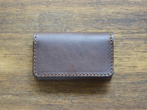 深棕色皮革製成的職人手作Organ名片夾，以咖啡色車線縫合邊緣，置於木紋桌面。