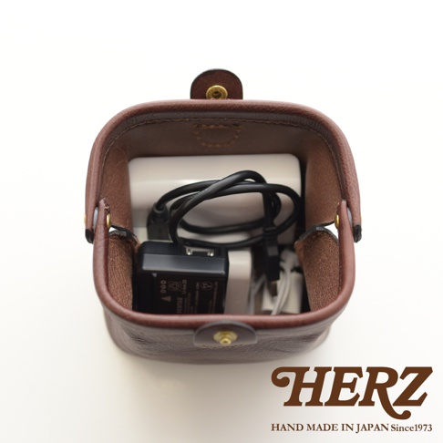 職人手作皮革口金化妝包 KF-143 M，深棕色皮革，內部裝有充電器和線材，包包的頂部有金屬釦。