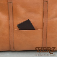 職人手作皮革包，呈現自然紋理的淺棕色皮革，包身設有外插袋，內有一張深棕色卡片。