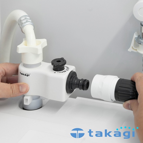雙手正在安裝 Takagi 洗衣機分水轉接頭，白色主體連接水管與黑色快速接頭，轉接頭上方配有調節水量的旋鈕，整體呈現簡潔的白色與黑色配色，展現直觀的操作過程。