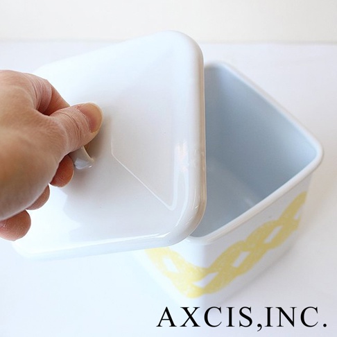 白色琺瑯方形收納盒，帶有黃色編織紋飾，盒蓋由手拿起，露出內部。