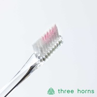 透明塑膠手柄牙刷，刷頭部分有白色和粉色軟毛，刷毛呈現傾斜角度。