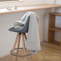 淺灰色絨面保暖毯，一角疊放在灰色布藝高腳椅上，毯子邊緣有淺藍色滾邊，毯子上帶有品牌標籤。