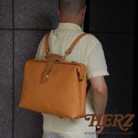 職人手作皮革軟式杜勒斯包，採用棕褐色牛皮製作，包包設計簡約，配有頂部提把、可調節肩帶及金屬扣環。