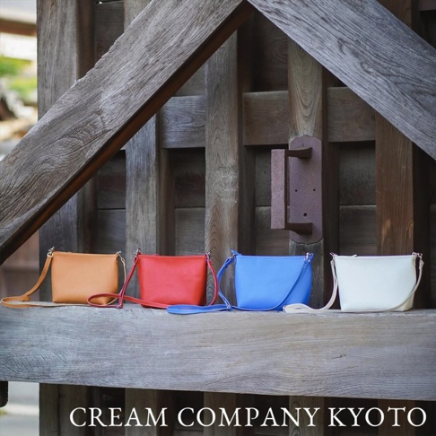 四款皮革隨身側背包，顏色分別為橘色、紅色、藍色及白色，皆配有同色系長背帶。