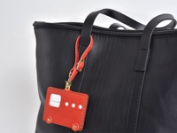 職人手作皮革可調式吊掛帶 (KZ-4)，紅色皮革製成，造型為小巴士，附有金色釦環和可調式掛繩，吊掛於黑色皮革托特包上。