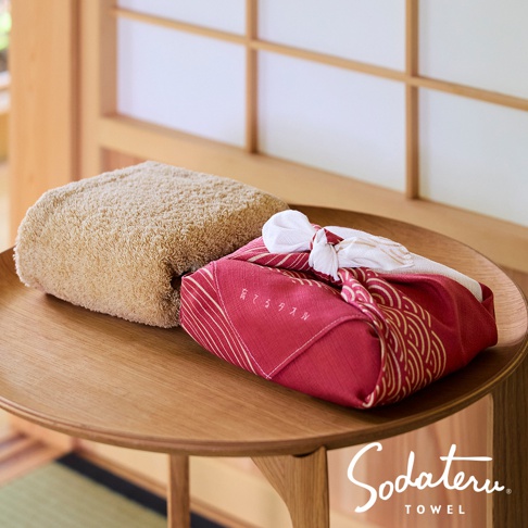 養育 TOWEL 和緣紋樣風呂敷毛巾，搭配一條未包裝的淺褐色毛巾，擺放在木桌上，背景為日式拉門。