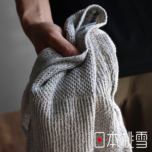 日本人手拿一條灰白色鬆餅紋連帽浴巾，浴巾的紋理細膩，邊緣有縫線。圖片右下方印有「日本桃雪」的品牌標誌。