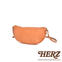 日本HERZ職人手作皮革半圓馬鞍包，棕褐色牛皮材質，呈現自然光澤與溫潤質感，簡約半月形設計，搭配金色拉鍊與金屬配件，展現精緻工藝。