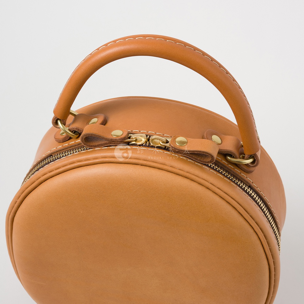 日本HERZ職人手作皮革兩用圓形包 Q-13 棕色，特寫圓形包的提把、拉鍊和側邊細節，有SUZUKI SHOP的浮水印。