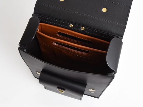 職人手作黑色皮革直式收納袋中袋，內部有兩個棕色皮革隔層，袋蓋處有金色釦件。