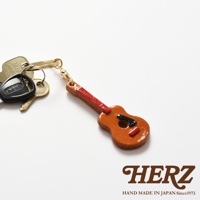 職人手作皮革吉他造型鑰匙圈，主體為棕色皮革，吉他琴頸為紅色，琴身點綴黑色與紅色裝飾。