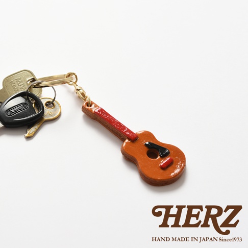 職人手作皮革吉他造型鑰匙圈，主體為棕色皮革，吉他琴頸為紅色，琴身點綴黑色與紅色裝飾。