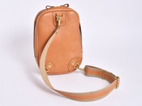 一個棕褐色皮革立體運動斜背包，配有可調節的帆布肩帶和金色金屬扣環。