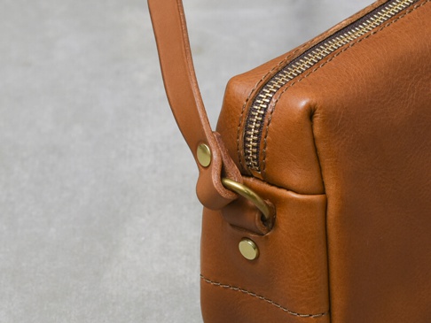 職人手作皮革Organ輕巧拉鍊單肩包 (G-80) M，採用溫暖的棕色皮革製成，搭配復古金色拉鍊與金屬扣環，展現精緻工藝與耐用質感。