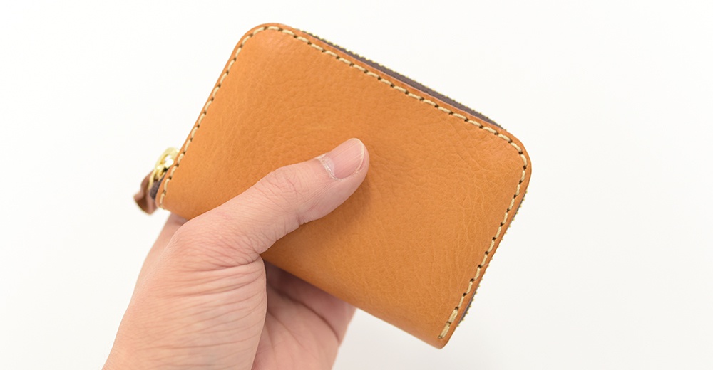 手持式淺棕色皮革拉鍊錢包，展示其精緻縫線和金色拉鍊頭。