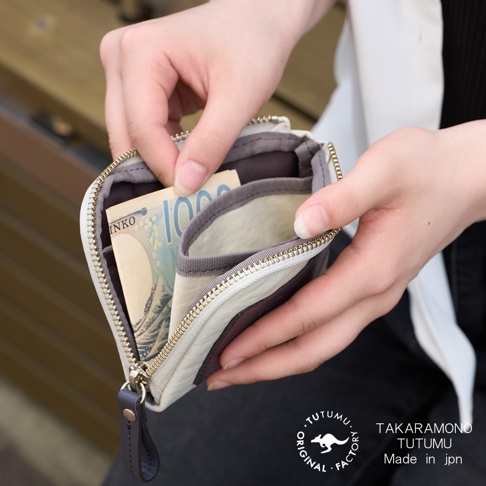 一隻手正在打開一個迷你錢包，裡面露出日幣鈔票，錢包上有「TUTUMU」的標誌。