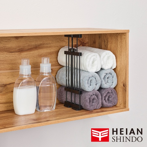 木製層架上擺放著兩瓶液體分裝瓶和一個黑色的毛巾架，架上整齊地捲著三層不同顏色的毛巾。