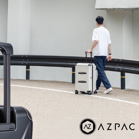 一名男子推著一個奶油色帶有黑色條紋的 AZPAC 行李箱走在路上。