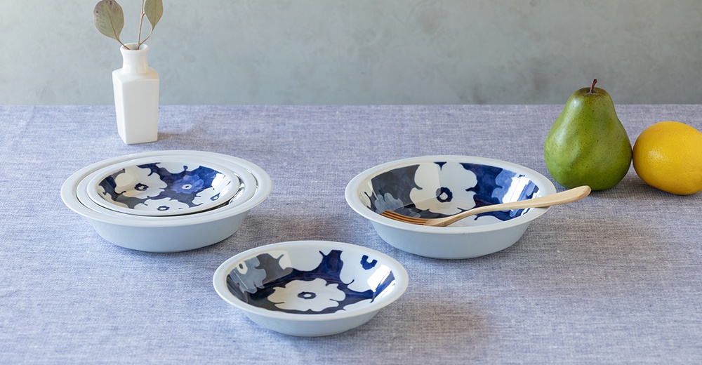 波佐見燒藍花紋四件式深碟盤組，包含三個不同尺寸的淺碗，內側飾有藍色花紋，外側為白色。盤組擺放在淺藍色桌布上，旁邊有綠色梨子和黃色檸檬。