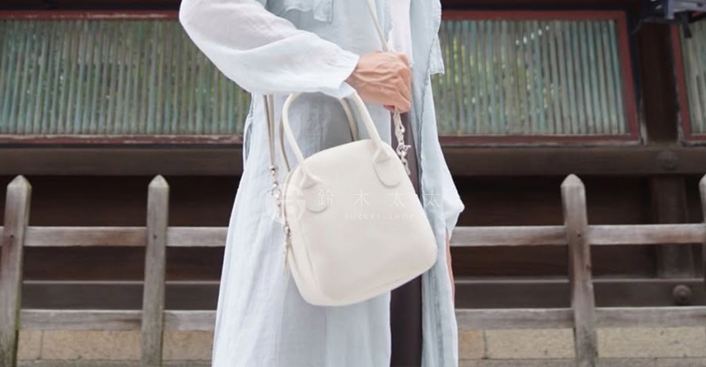 象牙白皮革貝殼造型手提包，配有可拆卸肩帶，由一位身穿淺藍色長袍的人士展示。