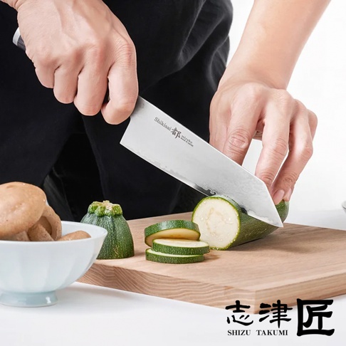 Shikisai Miyako 文化刀，刀身採用不銹鋼材質，帶有鍛造紋理。刀刃正在切割綠色櫛瓜，旁邊擺放著碗裝的香菇和切片的櫛瓜。