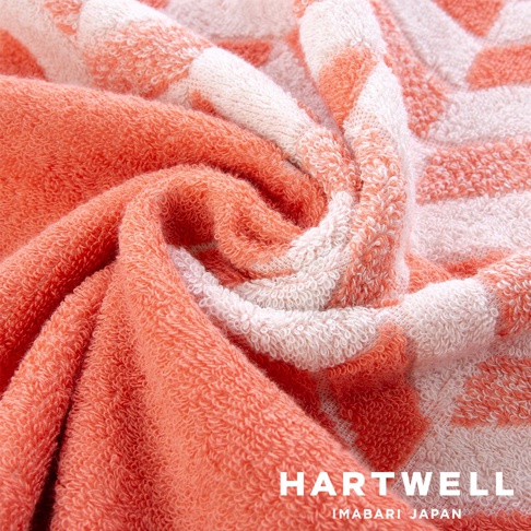 今治和風傳統紋樣言織毛巾，採用柔軟親膚的棉質材質，呈現珊瑚橘與白色交織的幾何圖案，毛巾表面觸感蓬鬆，紋理清晰。