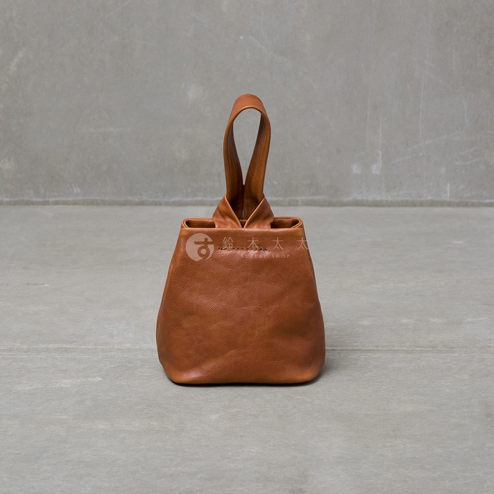 職人手作皮革Organ單柄手提包，採用柔軟的淺棕色皮革製成，包身呈水桶狀，上方有兩條交織的單柄提把，整體設計簡約。