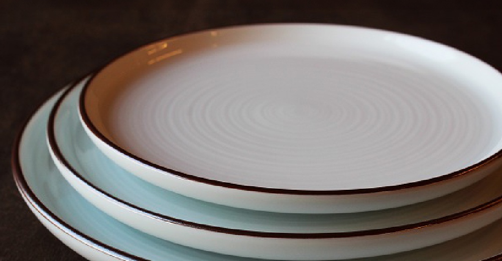 堆疊的白磁千段圓盤，最上方的盤子呈現同心圓紋理，盤緣帶有深色線條。下方盤子為淺藍色調，同樣帶有深色盤緣。