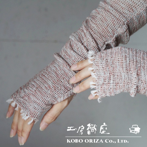 一雙粉紅色與灰白色交織的輕柔有機棉遮陽袖套，袖口有流蘇裝飾，展示於人手上。