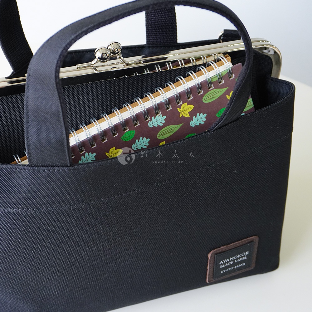 黑色手提包內有一個有葉子圖案的筆記本，包包上有一個金色口金開合，上面還有一個品牌標籤。