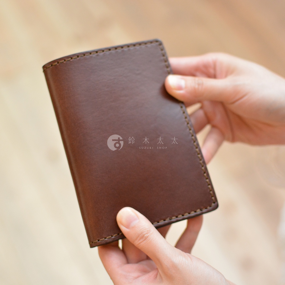雙手捧著一款咖啡色皮革經典護照套，細緻車縫線圍繞邊緣，皮革表面帶有自然紋理。