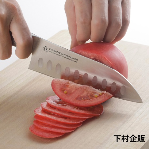 鉬釩不鏽鋼三德刀，刀身帶有凹槽，正切開一顆鮮紅番茄，番茄已切成多片薄片，置於木製砧板上。