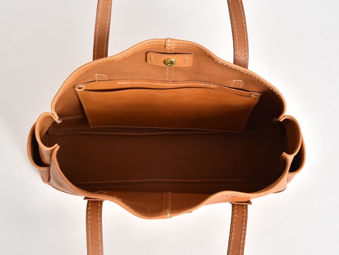 職人手作皮革橫式肩背托特包，呈現自然棕色調，採用真皮材質。包款內部有開放式隔層，外觀有簡約縫線設計，搭配雙肩帶。