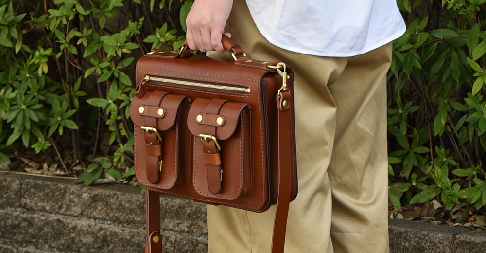 棕色皮革雙口袋兩用單肩包，配有金屬扣環和拉鍊，可手提或斜肩背。