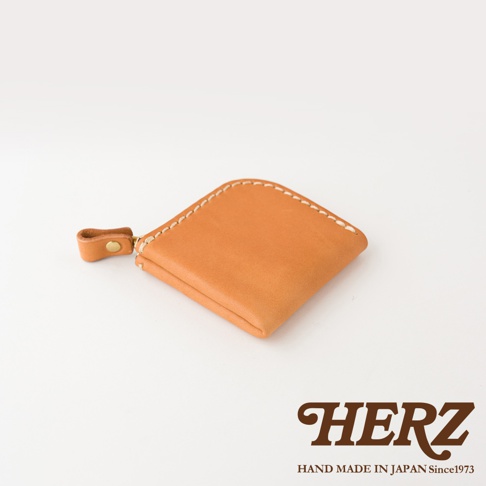 這款日本HERZ職人手作的淺棕色皮革分隔零錢包呈現側角視角，採用優質Stare皮革製成，表面具有細膩質感，邊緣以粗縫線手工縫製，側面配有一個裝飾性的小皮環與金屬釦，右下方印有HERZ品牌Logo與日本製造字樣。