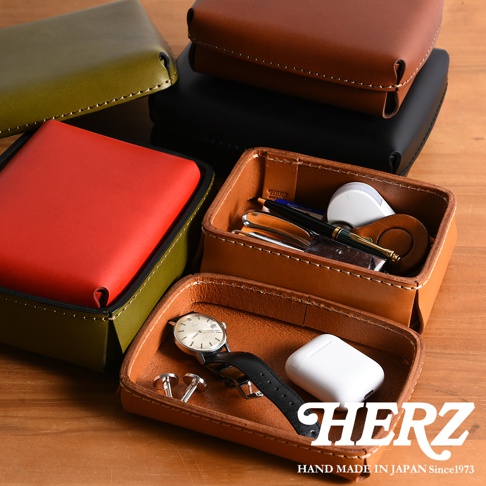 職人手作皮革小物收納盒，展示有綠色、紅色、棕色及黑色等不同顏色的收納盒，其中棕色收納盒內裝有筆、鑰匙圈、手錶、耳機及袖扣等配件。