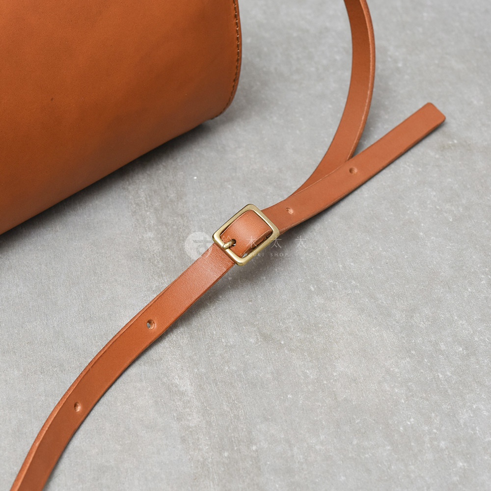 職人手作皮革Organ兩用口金手提包，淺棕色皮革，搭配金屬調節扣的長背帶，包體部分可見。