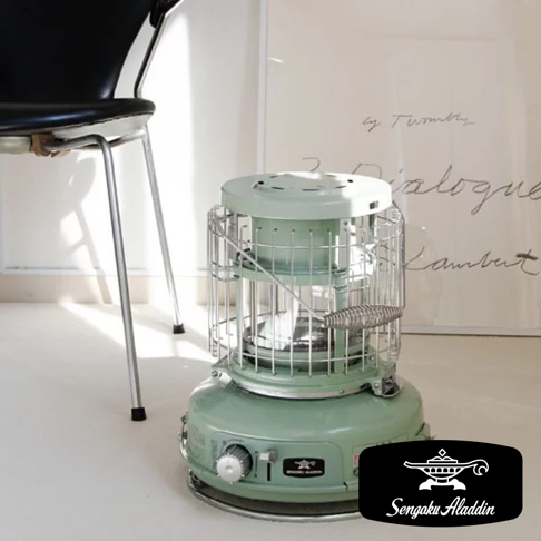 淺綠色卡式瓦斯暖爐，配有玻璃觀賞窗和銀色金屬防護網，頂部和底部為圓形設計，設有旋鈕和品牌標誌。