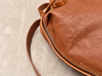 職人手作皮革後背包，呈現自然棕色，材質柔軟，表面有細緻褶皺紋理，搭配銅色金屬拉鍊，簡約設計。