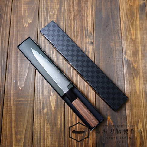 景清 Chromax 鋼水果刀，配有胡桃木握柄，刀刃呈現銀色金屬光澤，置於綠色襯墊的黑色長方形禮盒內，禮盒蓋為黑色格紋設計，整體擺放在木紋桌面。