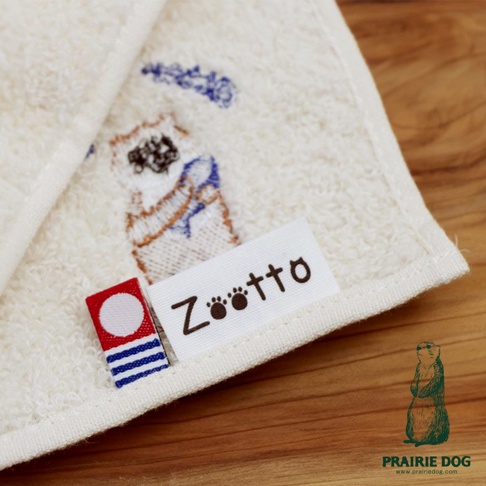 米白色精梳棉方巾，繡有卡通小狗圖案，並附有「Zootto」品牌標籤。