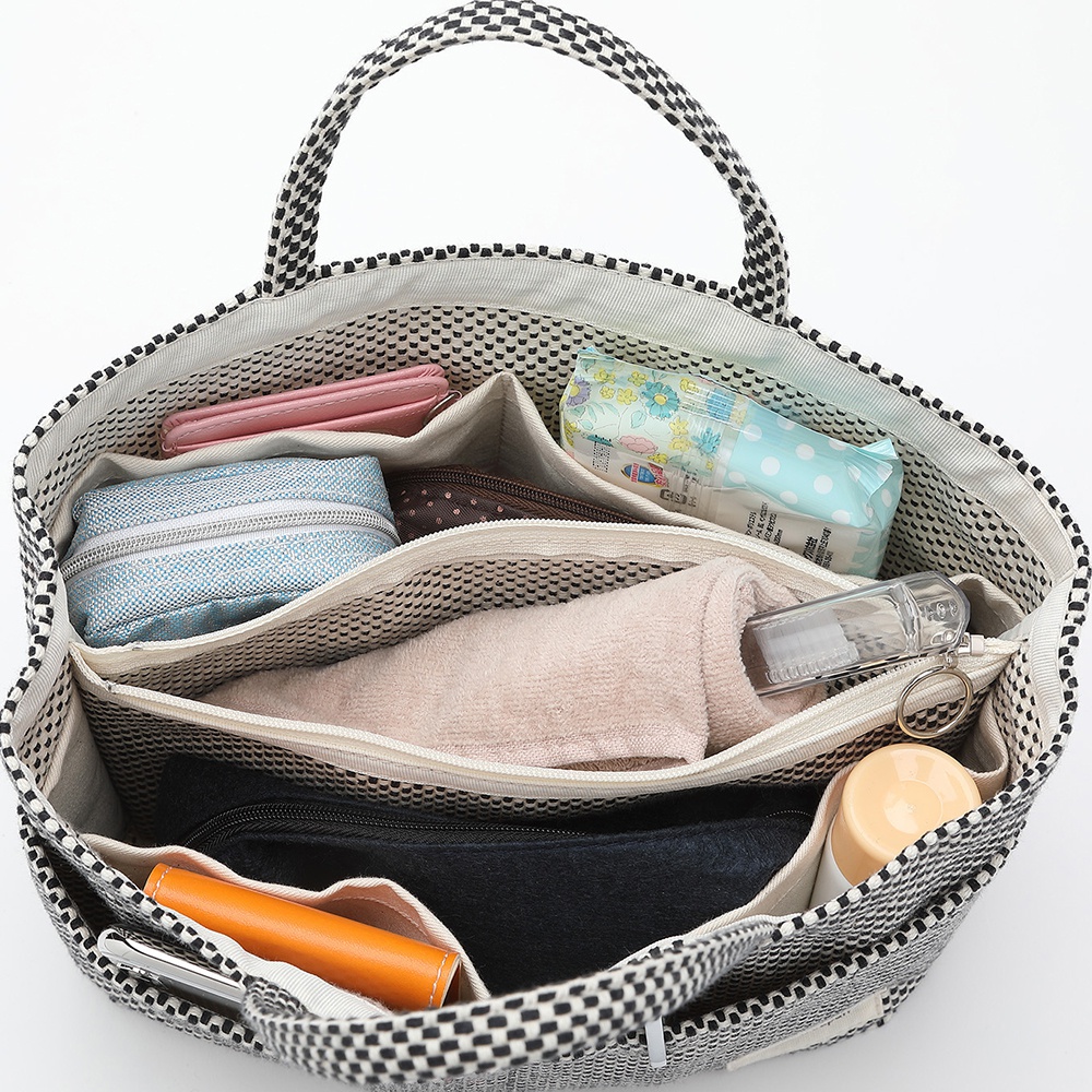 一個裝有粉紅色錢包、藍色化妝包、紙巾包、毛巾和牙刷的黑色與白色格紋托特包內部，有多個隔層和口袋。
