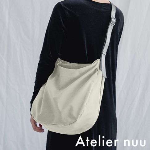 Atelier nuu ssent 肩背托特包，由一位模特兒展示，以淺米色為主色調，款式為柔軟廓形，搭配灰色可調節肩帶。