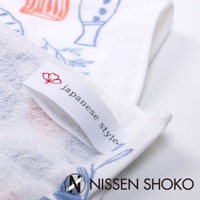 白色棉紗廚房拭巾，印有日式風格的藍色與橘色花卉及植物圖案。一條白色織帶標籤縫於拭巾上，印有紅色小花和「japanese style」字樣。